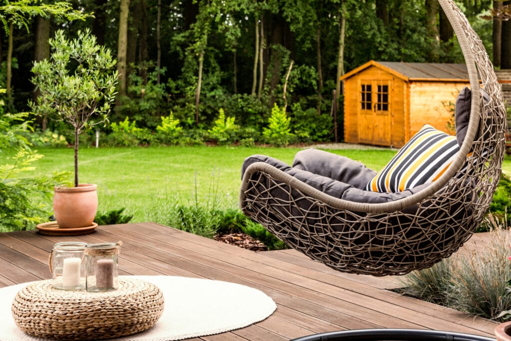 pouf on white round rug next to a hanging chair in the garden of a house