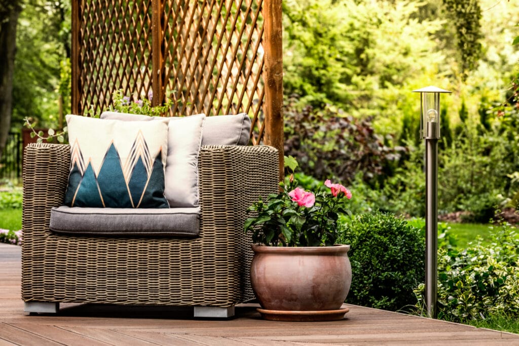 pink flowers next to a rattan armchair with decorative pillows on wooden terrace