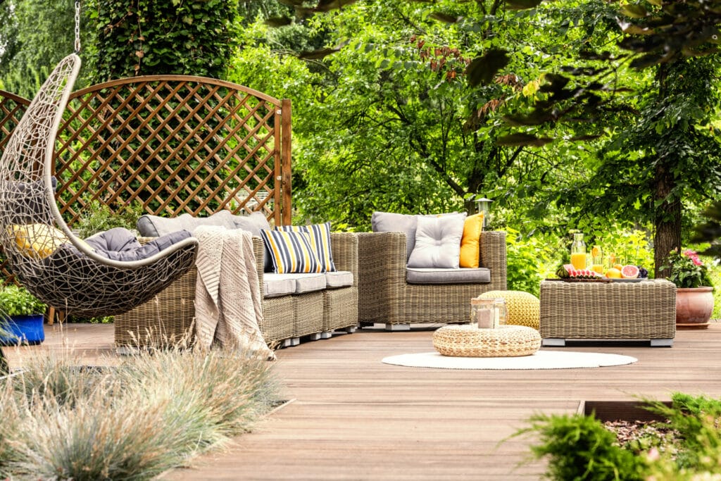 wooden veranda with rattan furniture, comfy swing and trees in the background